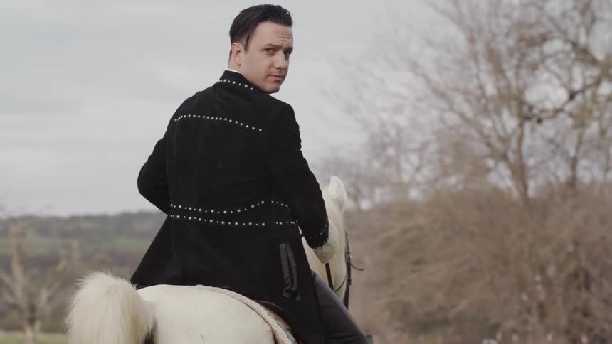 Man looks behind him as he rides a white horse in a field
