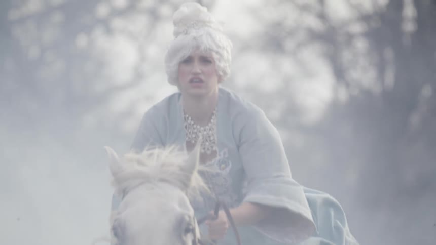 Woman wearing a white wig and dress rides a horse in a foggy field