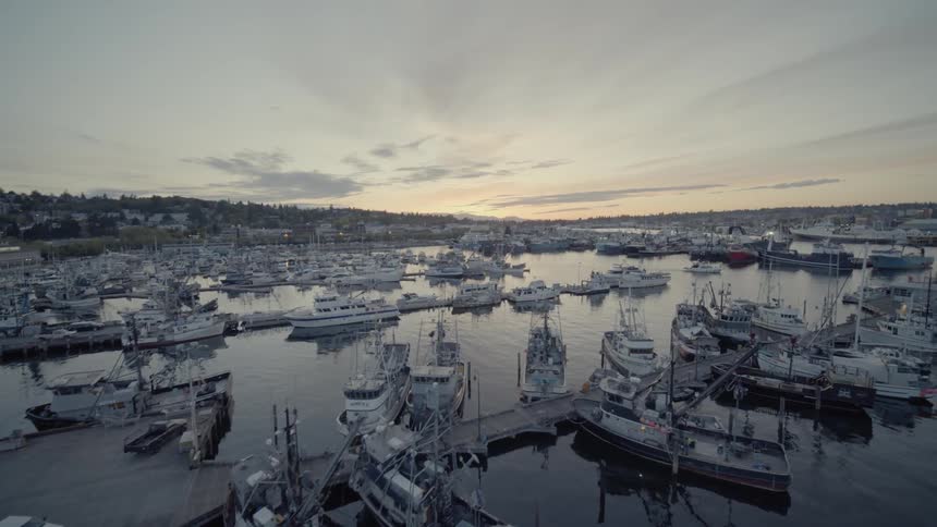 Ascending along work boats and yachts docked at a marina under a beautiful sunset sky
