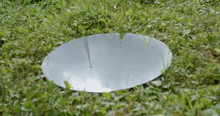 A mirror laying in the grass showing the clouds