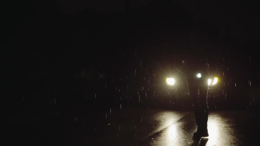 Person walks in front of car headlights on a rainy night