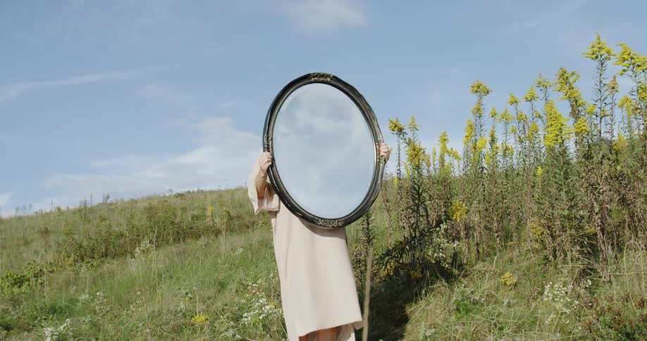Woman holds an oval mirror while standing in a field
