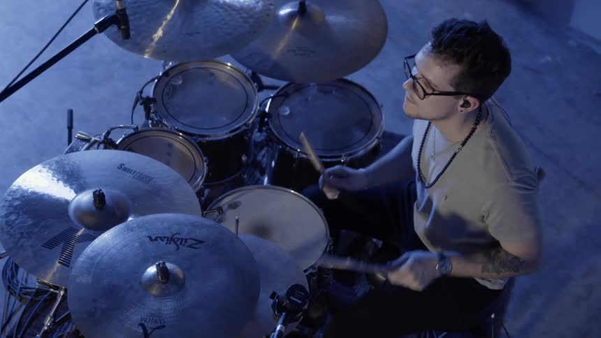 Man plays drums in a room illuminated by blue light