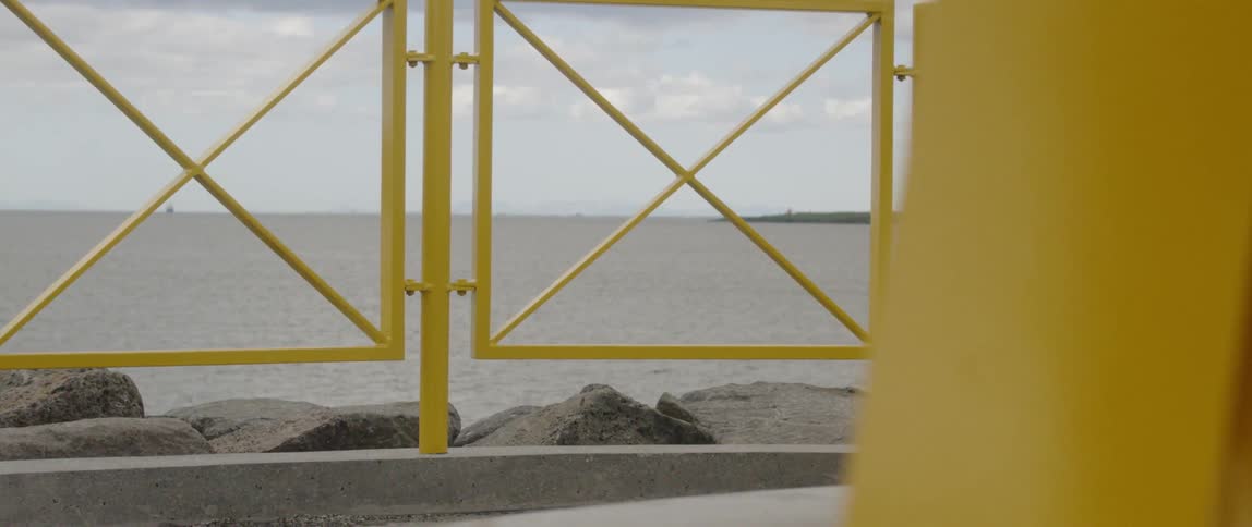 The tide is rolling in the ocean beyond a fenced walkway on a cloudy day