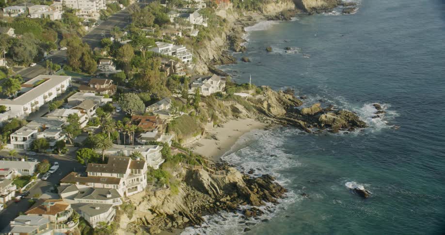 Waves crash into shore as buildings sit on a hill
