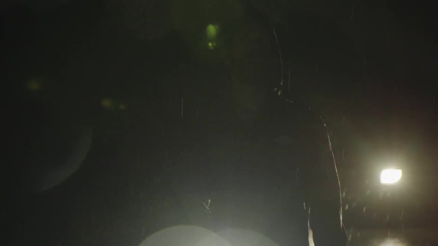 A man stands with a flashlight outside in the rain