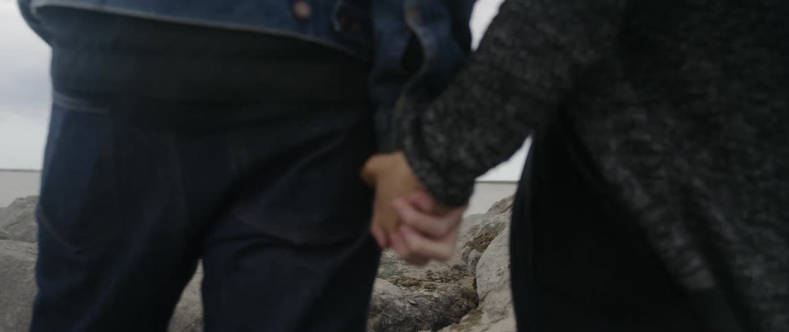 A couple are holding hands as they stand outside at the beach on a cloudy day
