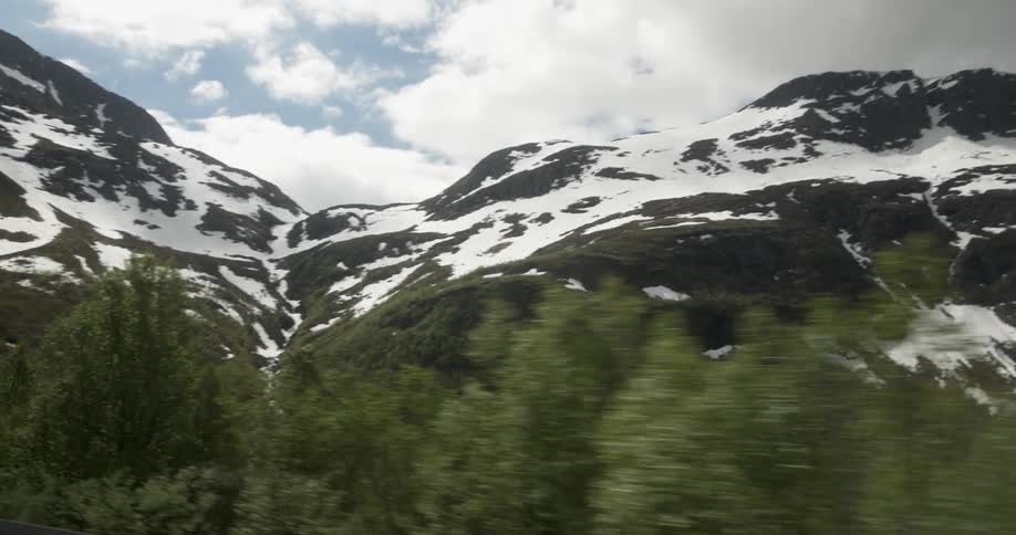 Travelling past a body of water with snow-capped mountains and fluffy white clouds in the background