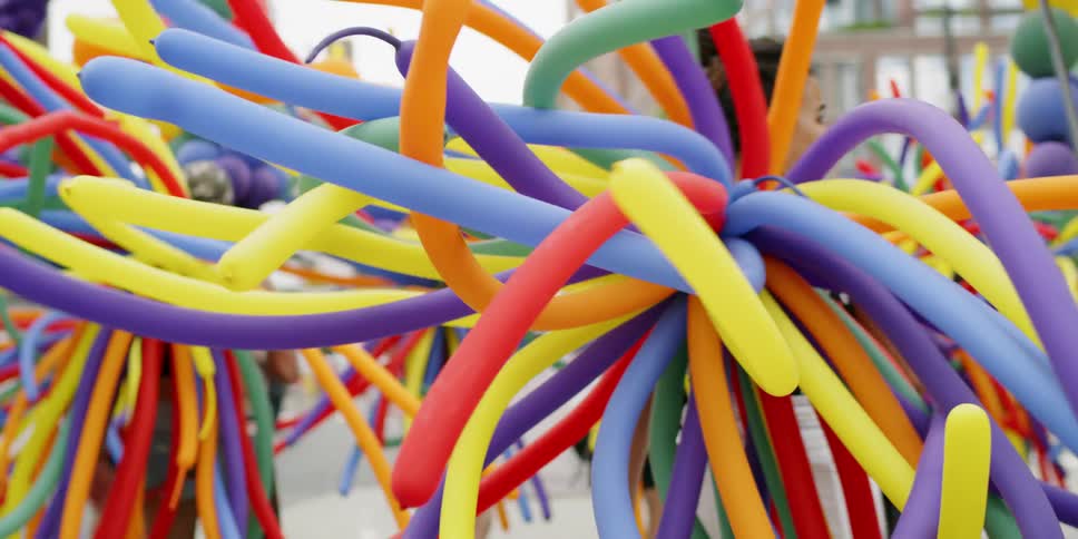 A group of people wearing balloon costumes is marching in a parade in daylight