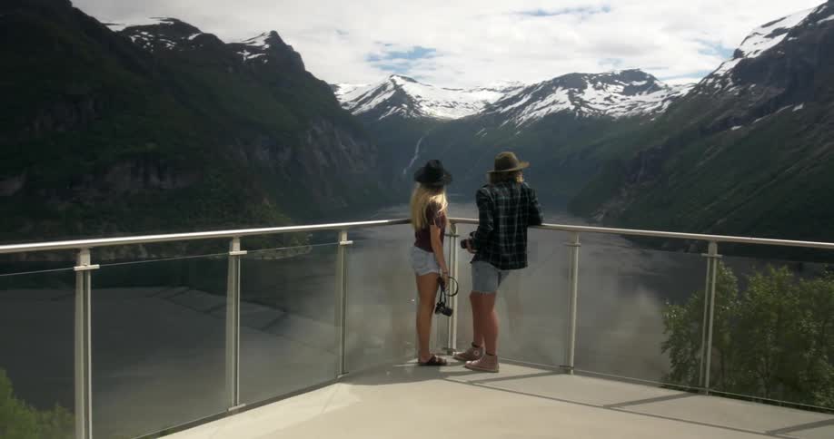 A man and woman look at snow capped mountains from an observation desk