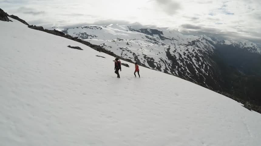 A man and woman walk up a snow covered mountain during the day