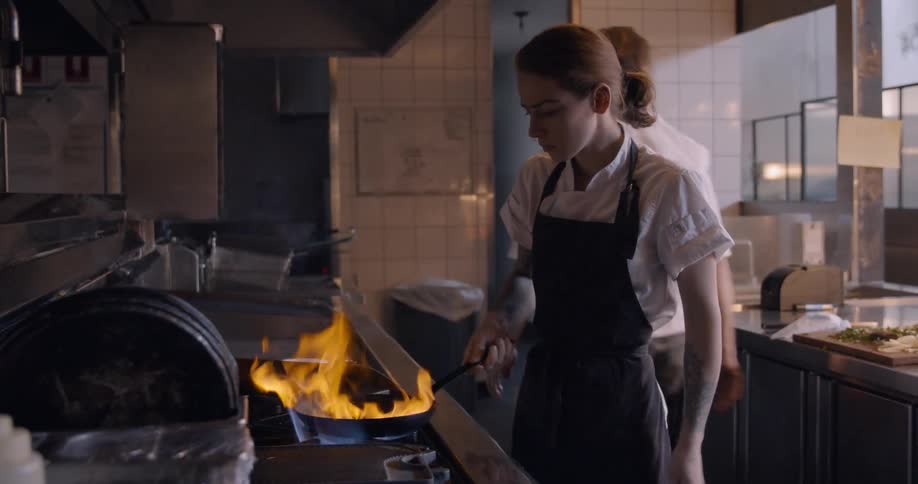 Woman cooks in a restaurant and flames surround the frying pan