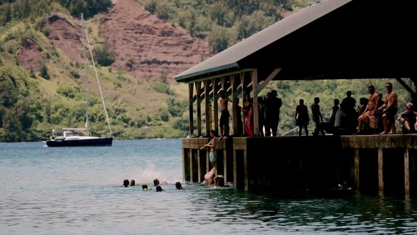 People jump off a dock into a mountain lake