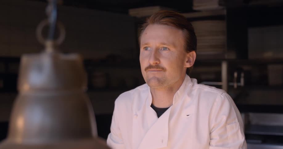 A chef stands in a dark kitchen