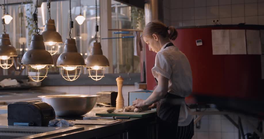 A female chef is working in a restaurant kitchen at dusk