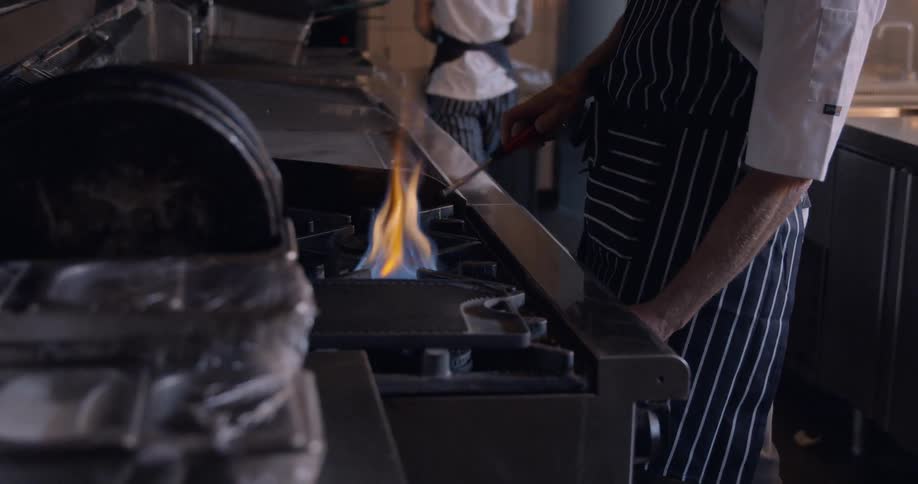 A chef turns the stove on in the kitchen