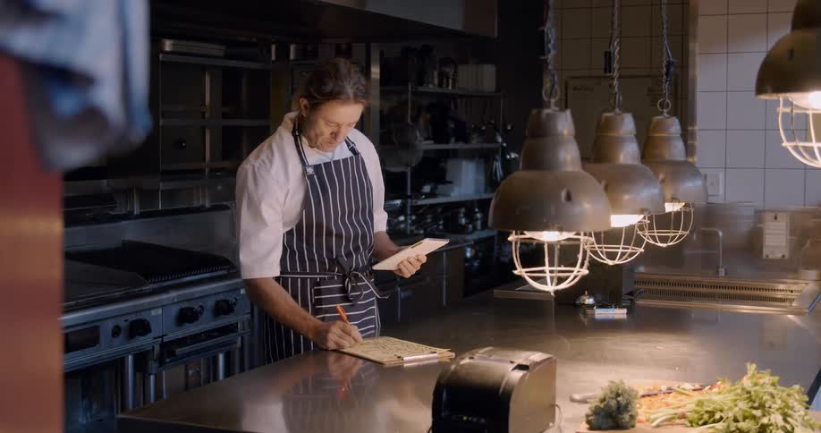 A chef writes down notes inside a kitchen