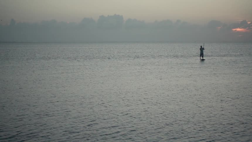 Man is paddle boarding on body of water at sunset