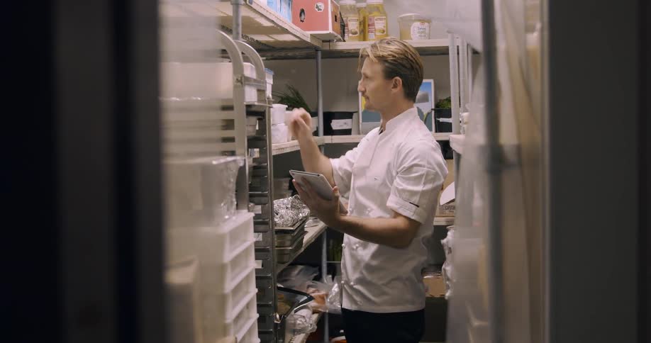 A chef takes inventory notes inside the restaurant cooler
