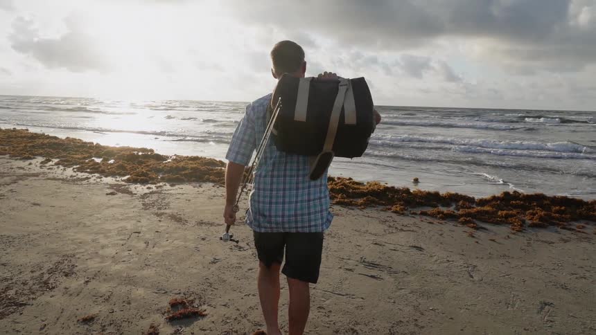 A man carries his bag and fishing pole onto the beach