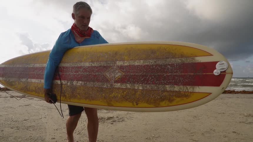 A man carries his large surfboard on the beach