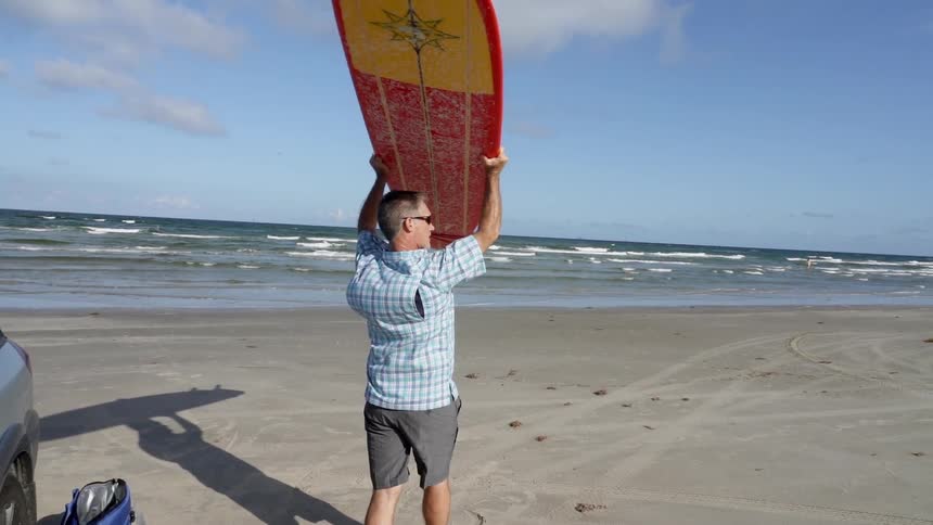 A man holds a surfboard over his head on the beach