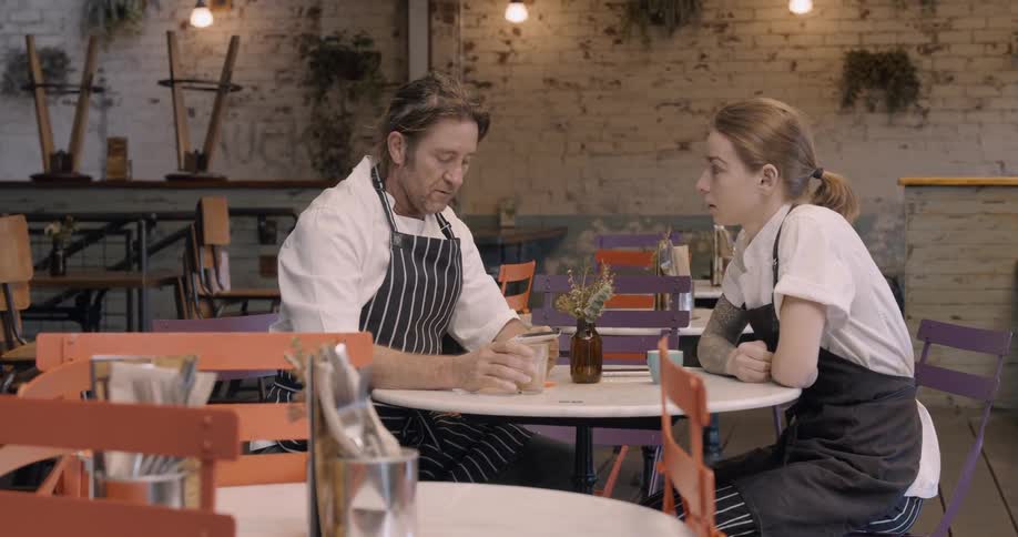 Two chefs sit and talk at a table