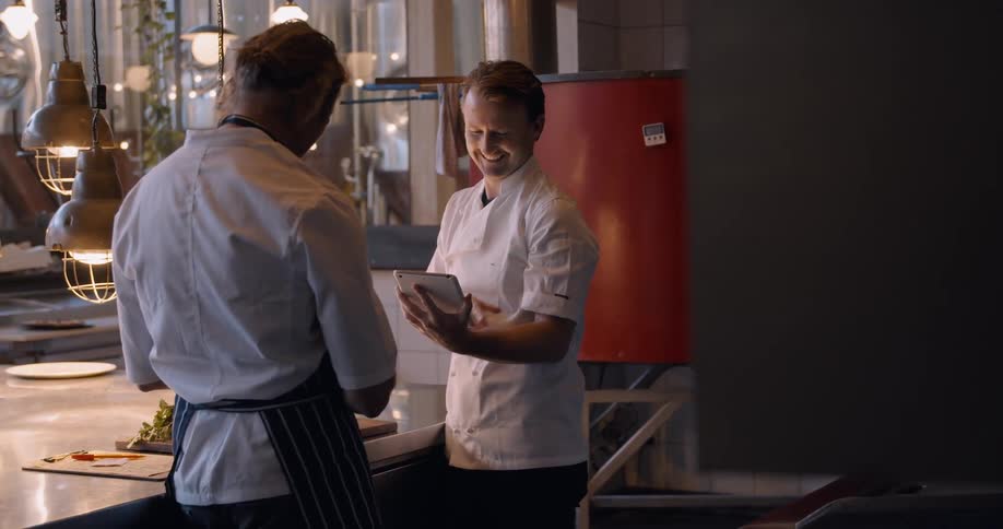 Two chefs talk in a restaurant kitchen