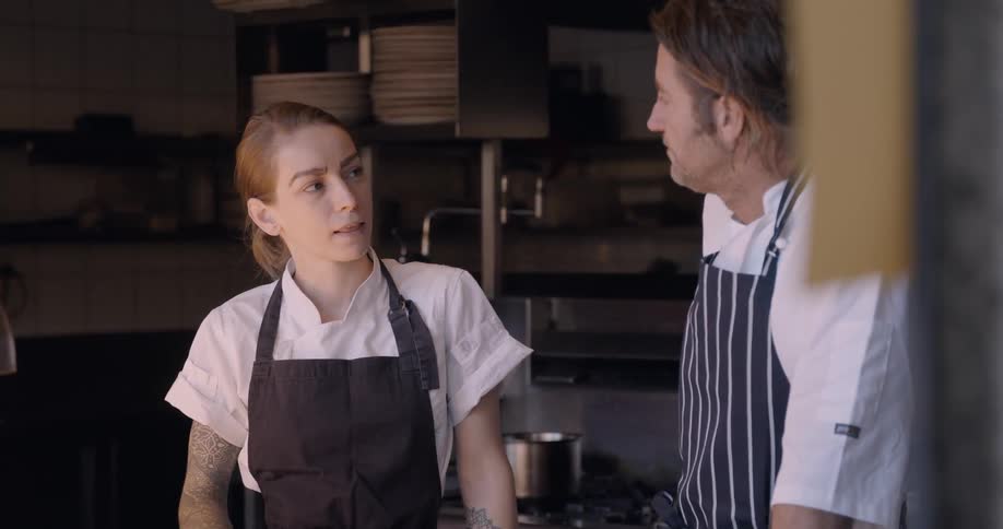 Two chefs talk in a restaurant kitchen