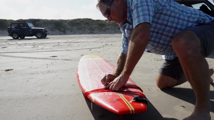 A man waxes a surfboard on a beach