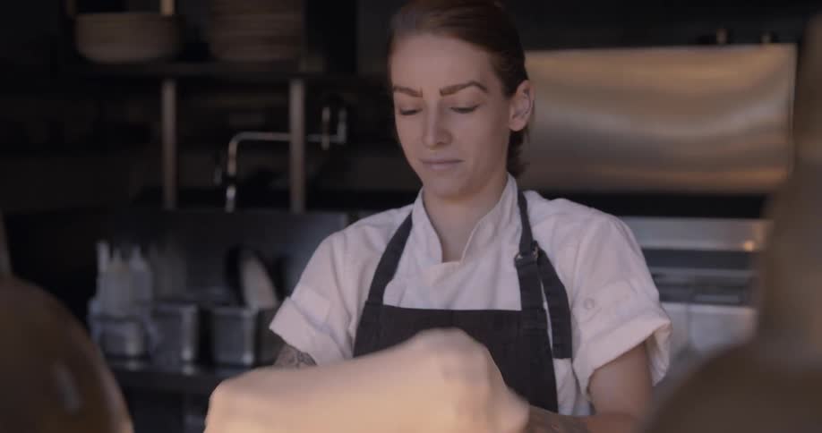 A woman is making pizza inside restaurant kitchen