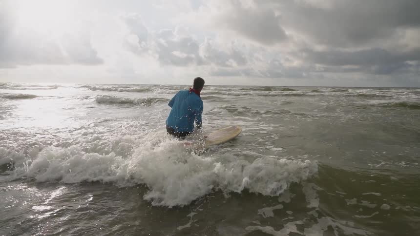 A man pushes a surfboard into the waves