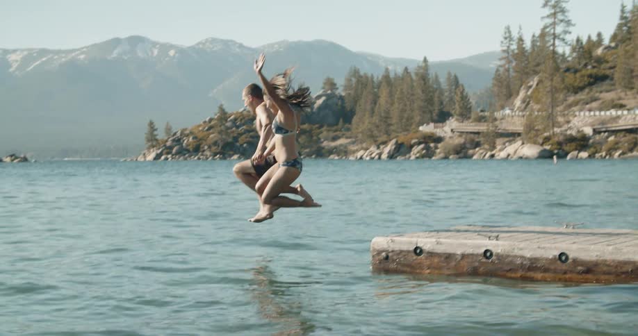 Man and woman run and jump off dock into lake on sunny day