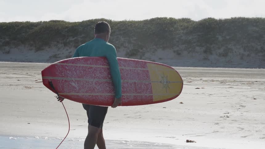 A surfer walks on a sandy beach