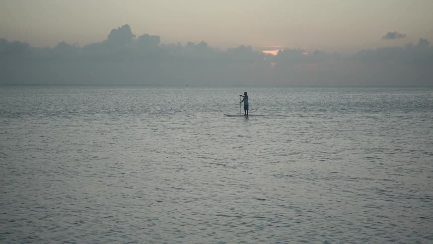 Person stands on a surfboard paddling in the ocean