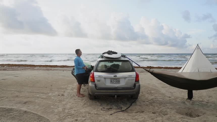 Man is standing next to car overlooking ocean on cloudy day