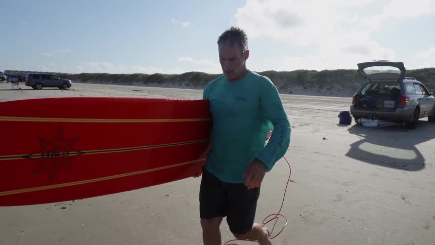 A surfer carries a surfboard on a beach