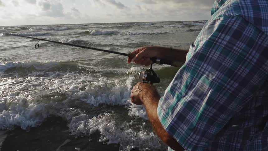 A man fishes on a beach on a cloudy day