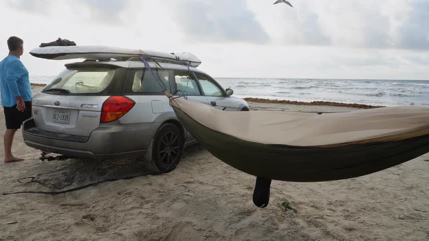 A hammock is strung between two cars on a beach