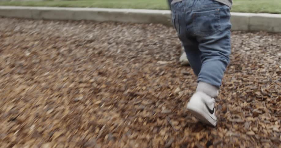 A toddler is running toward an adult outside in a park in daylight