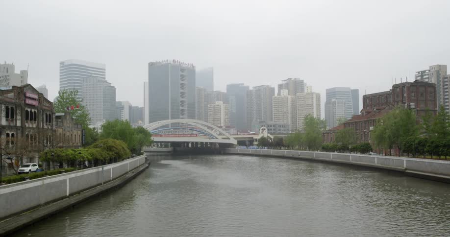 A river is running beneath a bridge in a city on a hazy day