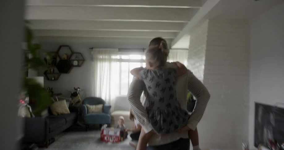 A father carries his daughter on his back at home