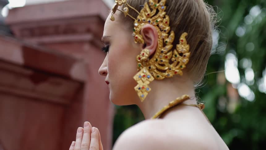 A woman prays while wearing ornate jewelry