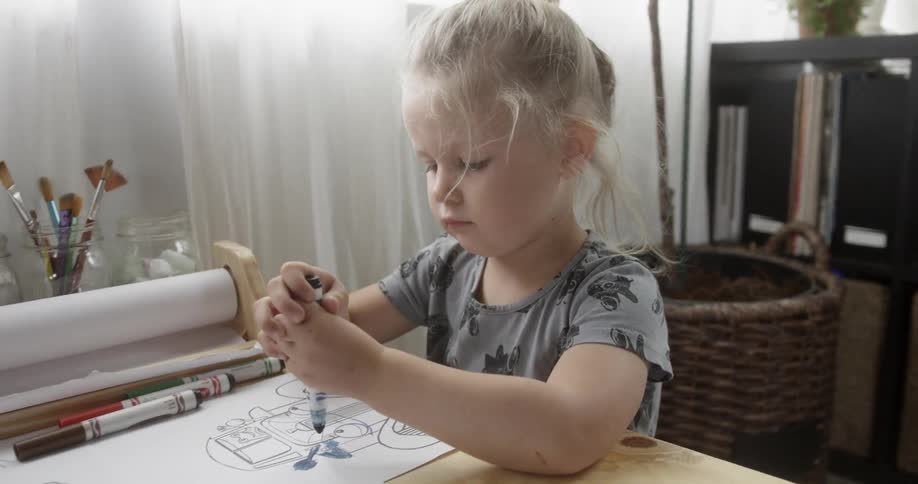 A girl is sitting at a table coloring inside a home during the day