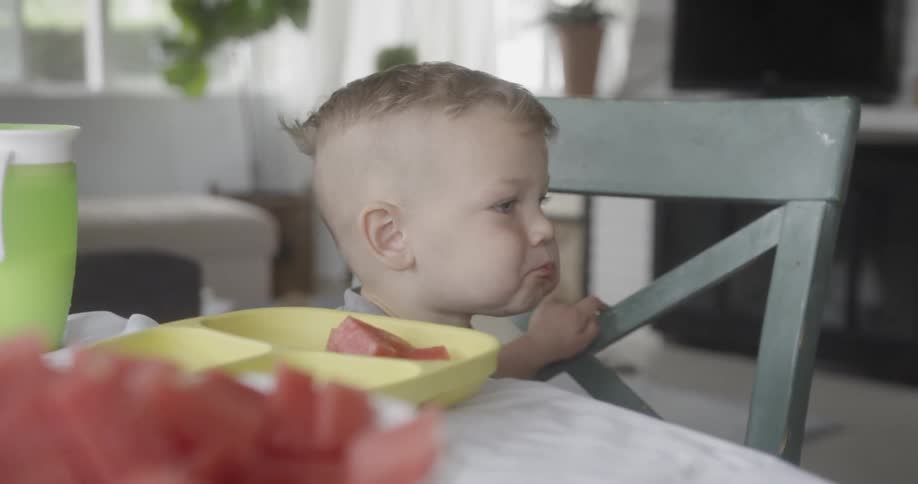A young boy eats watermelon at the table