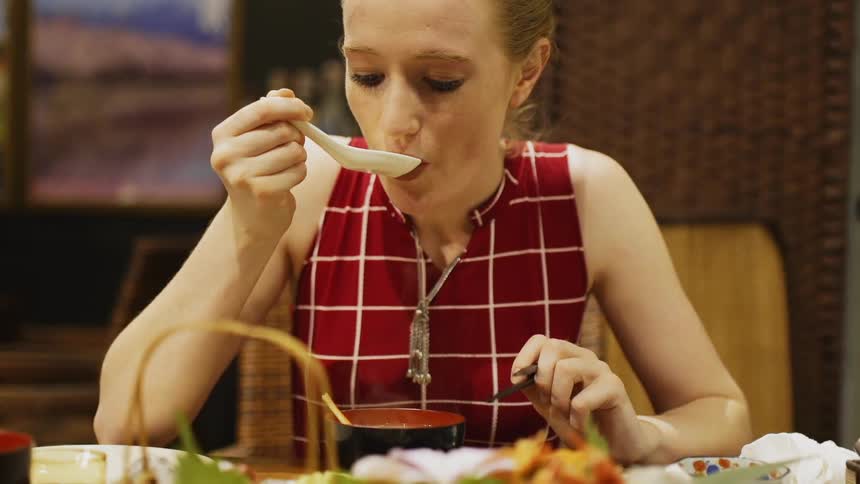 Woman uses a spoon to eat soup from a cup