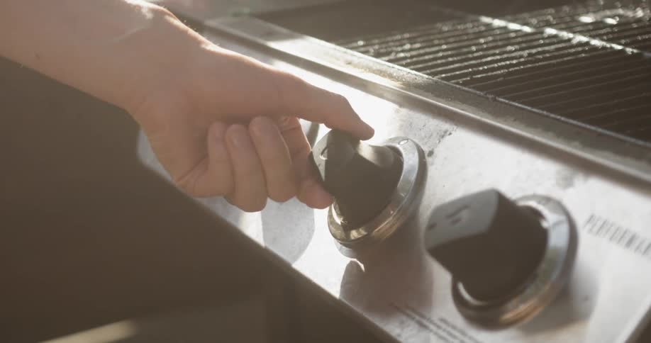 A person turns knobs on a grill