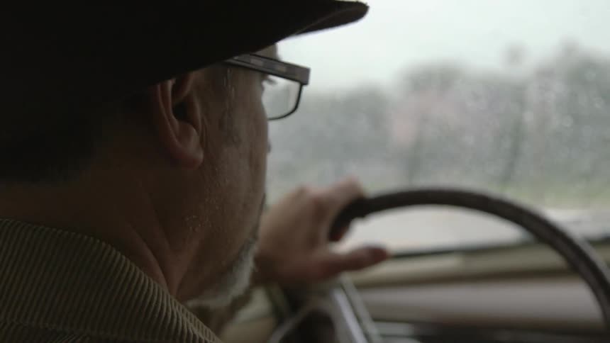 A man wearing glasses sits behind the wheel of a car