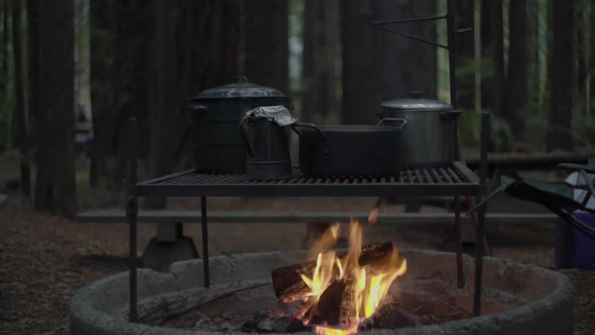 Pots and a coffee pot sitting on a grill placed over a campfire