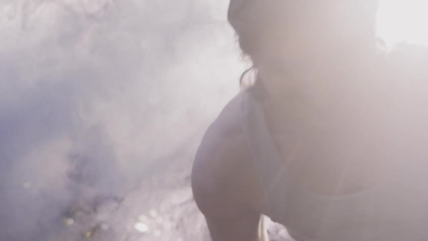 A man laughs as he dances through colored smoke on a sunny day